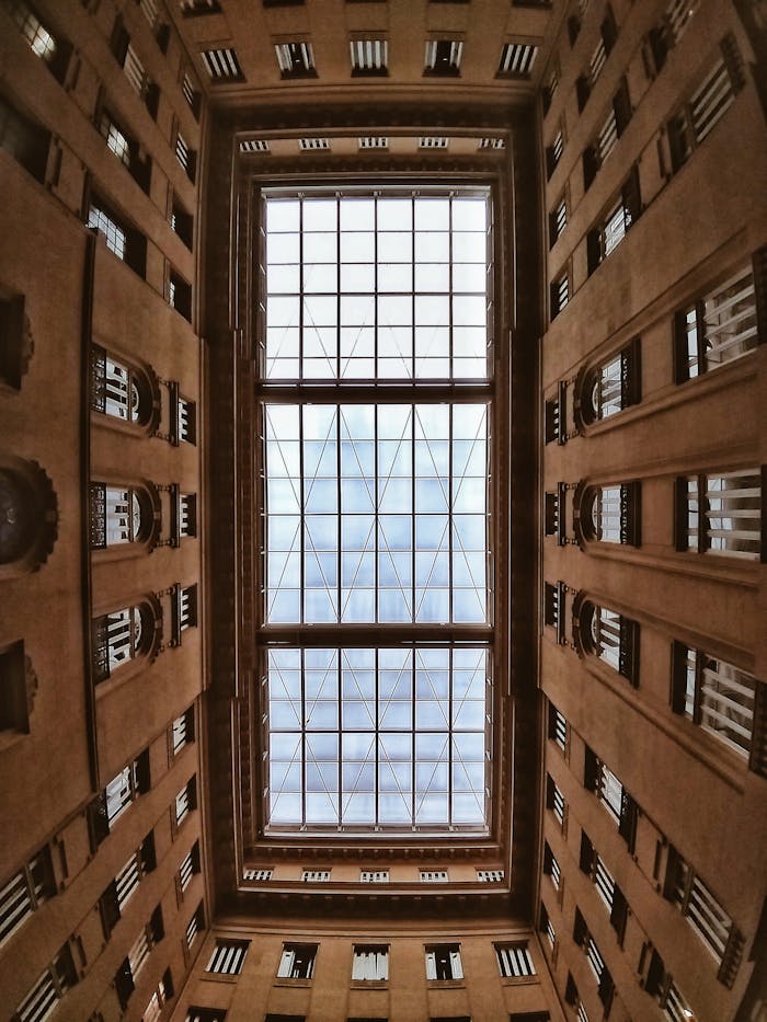 Contemporary architectural atrium featuring a large glass ceiling, viewed from below.