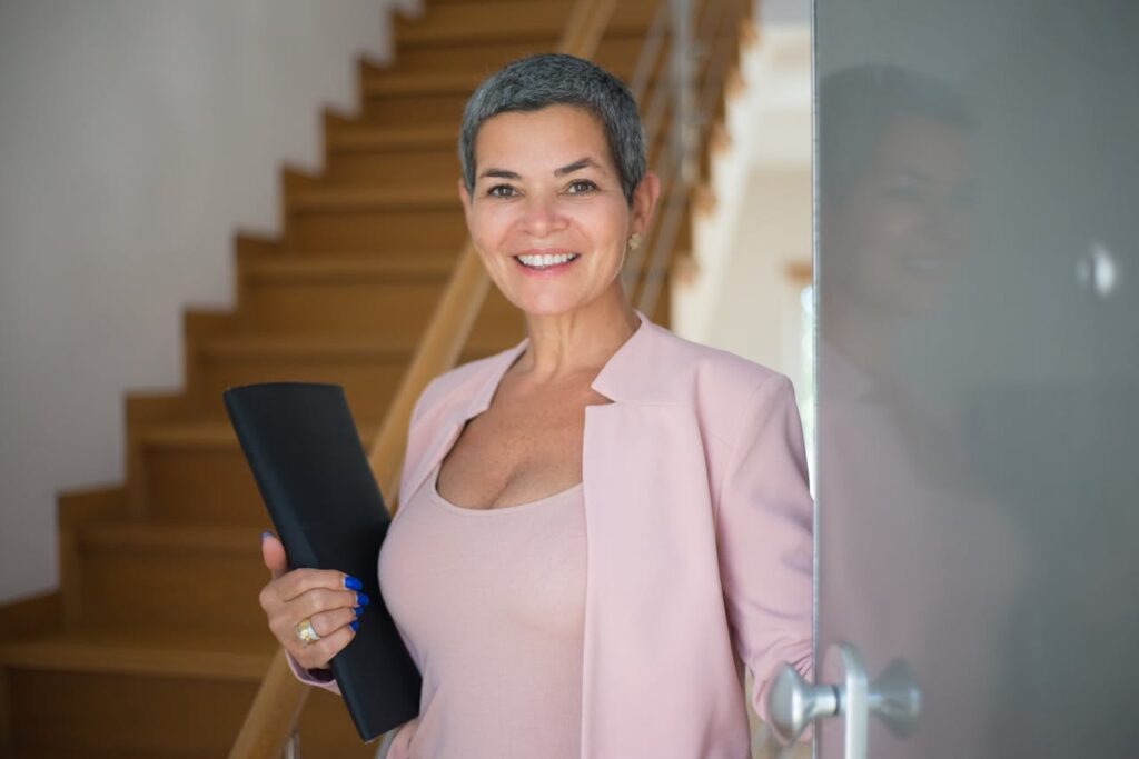 pexels-photo-8730034 Confident senior woman entering a modern office setting, holding documents and smiling.